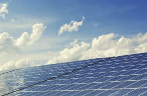 Solar panels installed in rows, angled toward the sun, with a bright blue sky and scattered white clouds overhead, representing renewable energy and power infrastructure planning.
