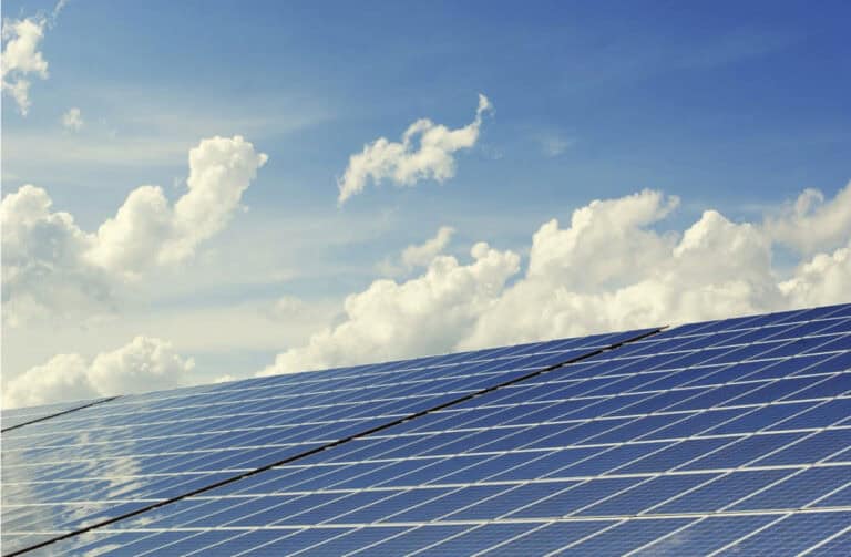 Solar panels installed in rows, angled toward the sun, with a bright blue sky and scattered white clouds overhead, representing renewable energy and power infrastructure planning.