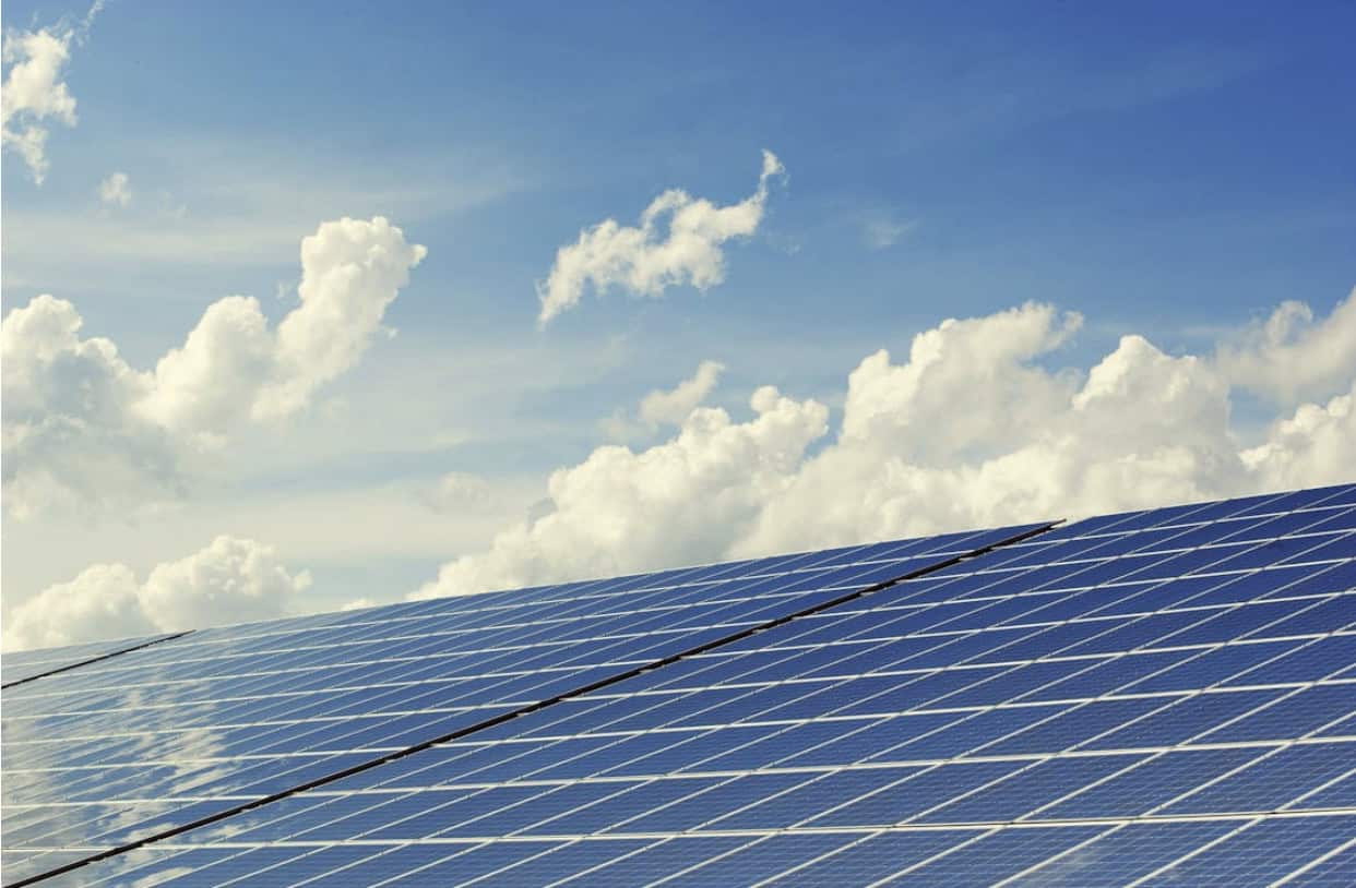 Solar panels installed in rows, angled toward the sun, with a bright blue sky and scattered white clouds overhead, representing renewable energy and power infrastructure planning.
