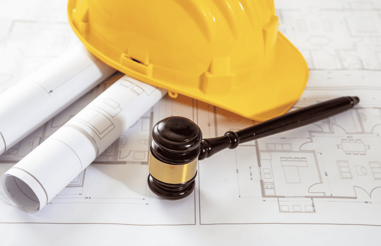 Judge’s gavel and yellow construction hard hat resting on architectural blueprints, representing construction law and building regulations.