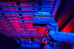 Close-up view of server racks and drive bays inside a mission-critical data center facility lit in red and blue, illustrating the infrastructure demands of high-uptime environments.